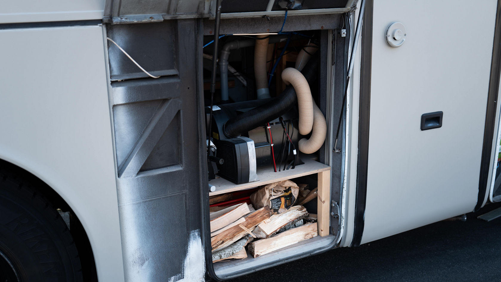 Espace de rangement ouvert sur la transformation de camping-car Setra gris avec technique, flexibles et bois de chauffage stocké sous le compartiment