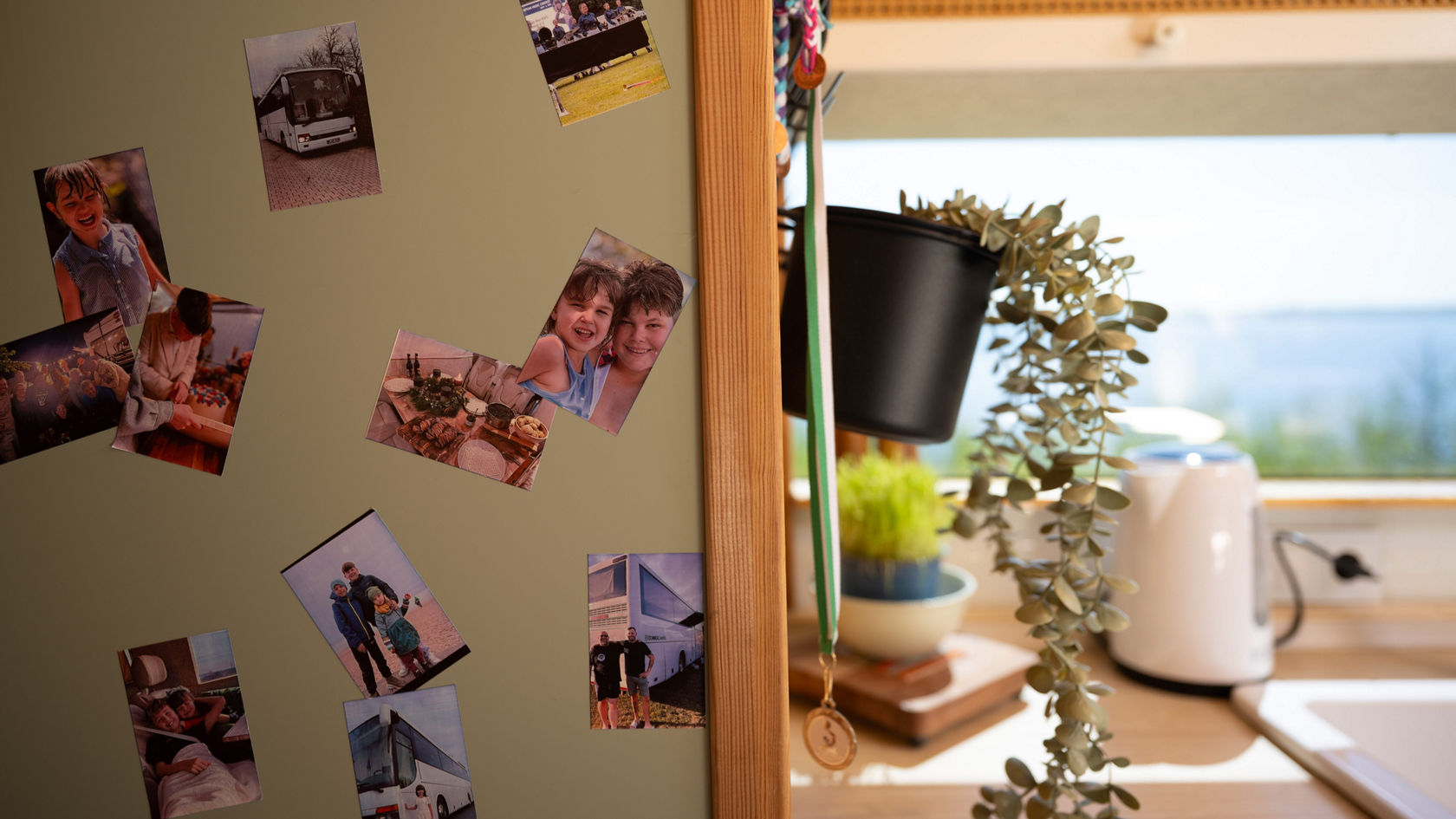 Gros plan sur la transformation d’un camping-car Setra : photos sur une façade d’armoire, plante suspendue et plan de travail de cuisine sur la vitre