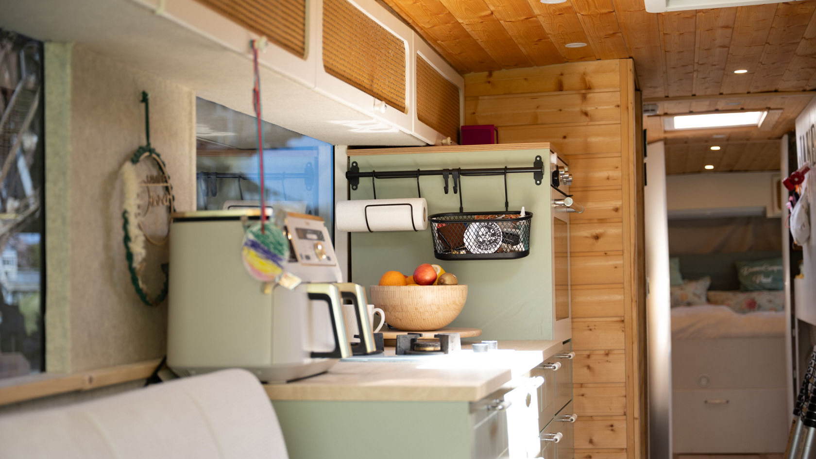 Kitchenette dans la transformation camping-car Setra avec plaque de cuisson, placard supérieur, bac à fruits et vue sur la zone de couchage