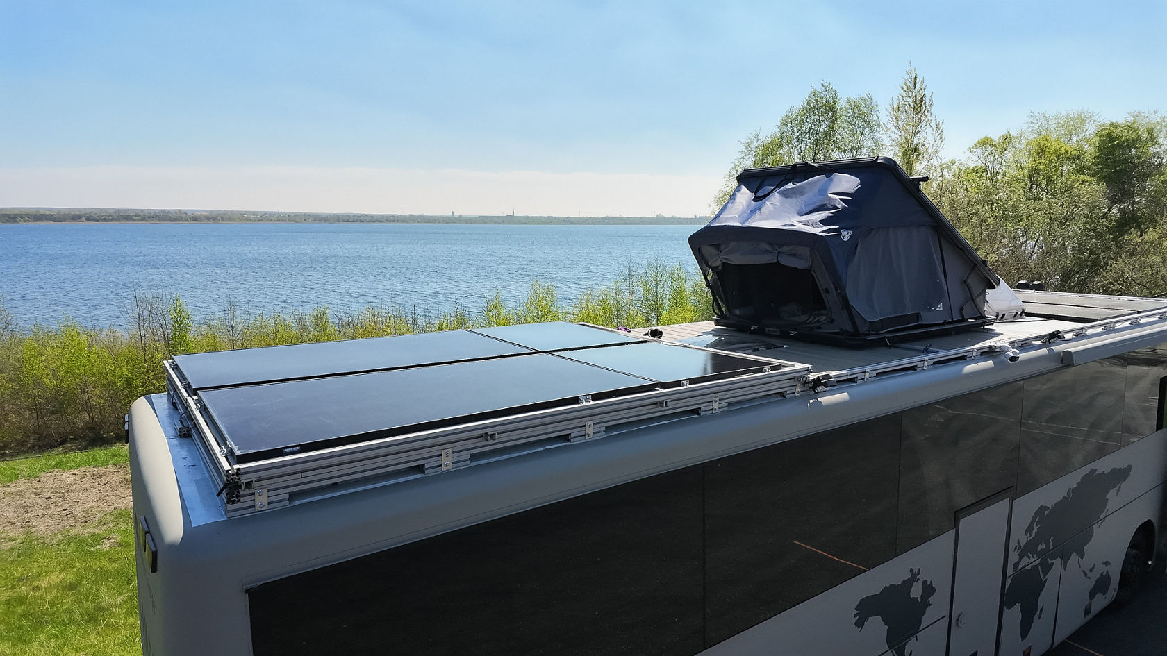 Toit d’une transformation de camping-car Setra avec panneaux solaires et tente de toit au bord du lac, vue sur l’eau