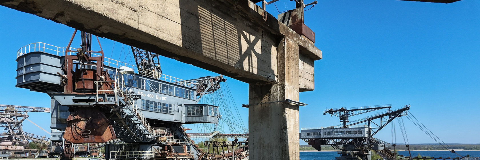 Paysage industriel avec de grandes pelles et une passerelle en béton devant un ciel bleu, lac en arrière-plan