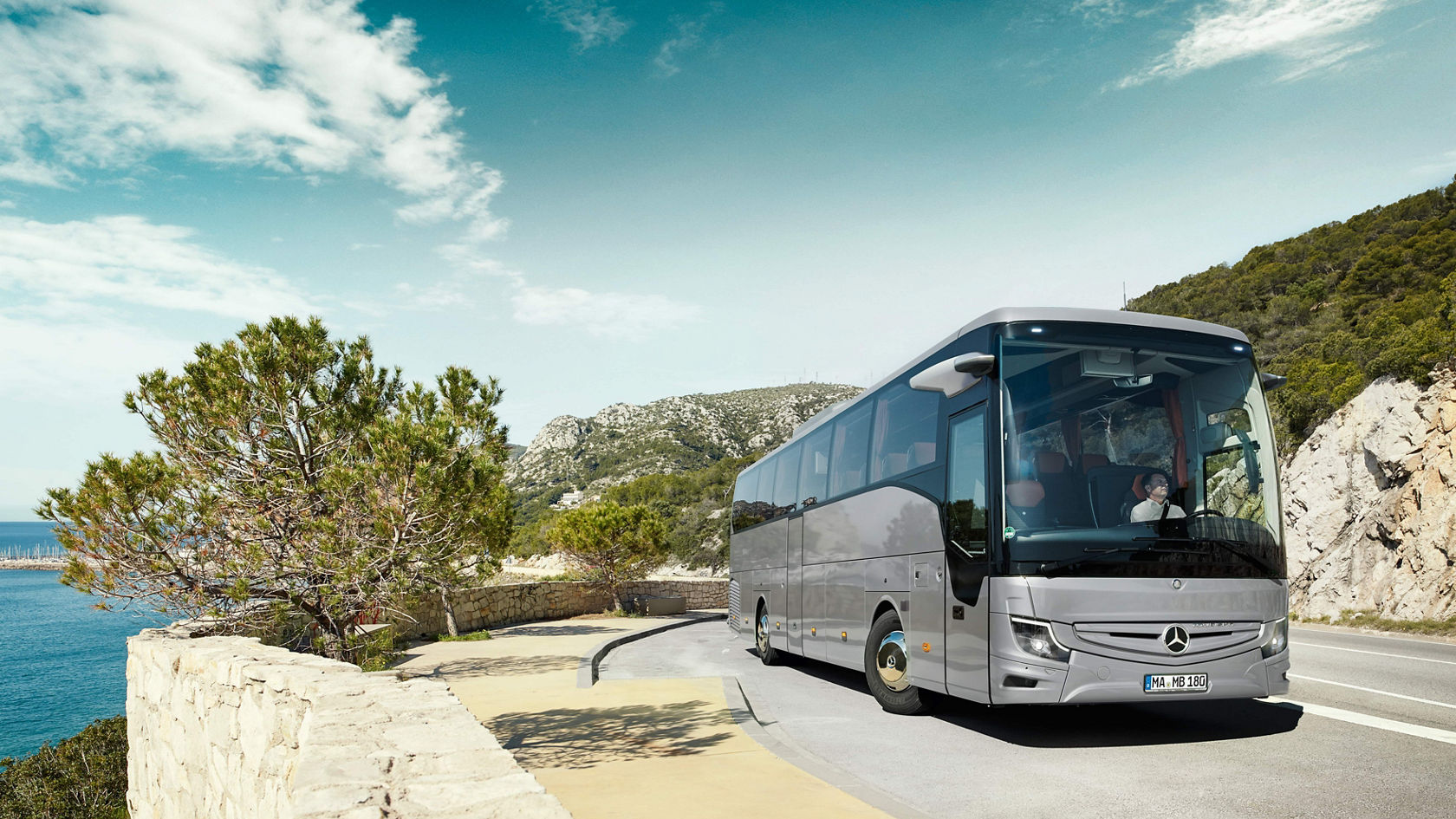 Mercedes-Benz Tourismo touring coach on a winding coastal road along rocks and sea under a blue sky