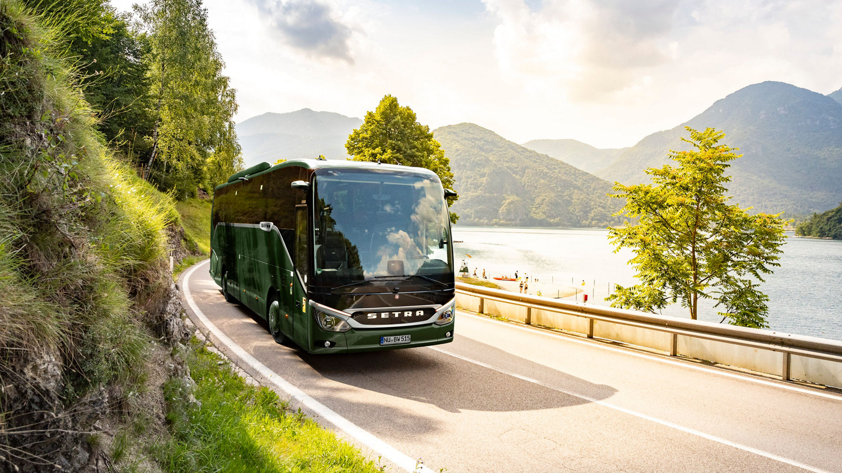 Green Setra ComfortClass touring coach driving on a winding coastal road along steep rocks, on the right a body of water