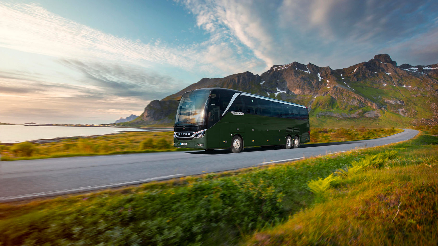 Green Setra TopClass 500 touring coach on a country road in front of a mountainous panorama and coastal landscape