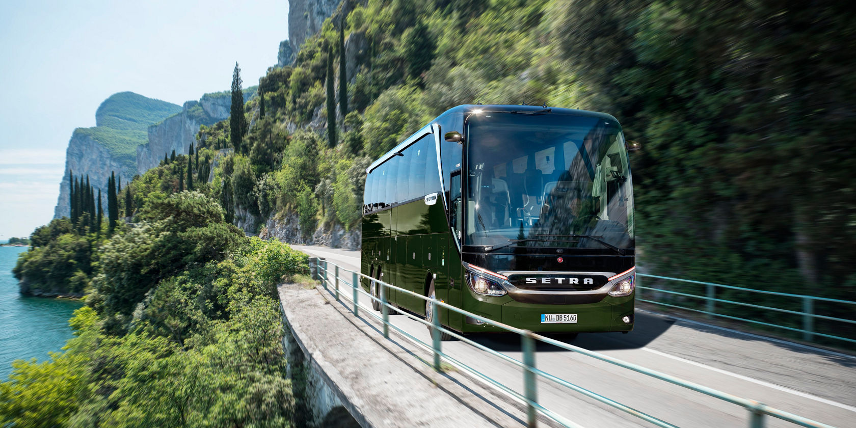Un autobus da turismo Setra TopClass verde percorre una stretta strada costiera lungo un lago davanti a ripide pareti rocciose