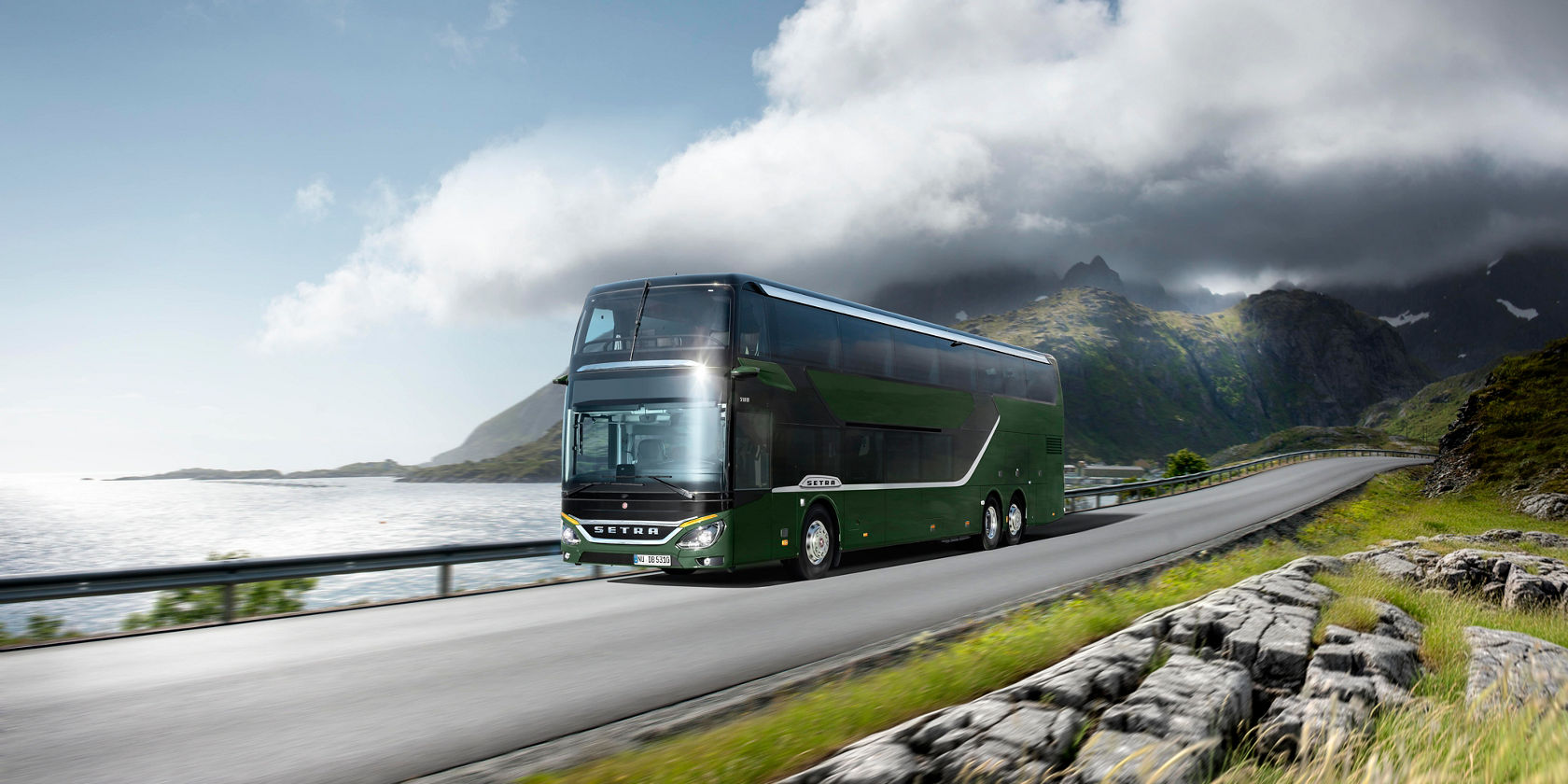Grüner Setra S 531 Doppelstock-Reisebus fährt auf Küstenstraße vor Bergen und tief hängenden Wolken