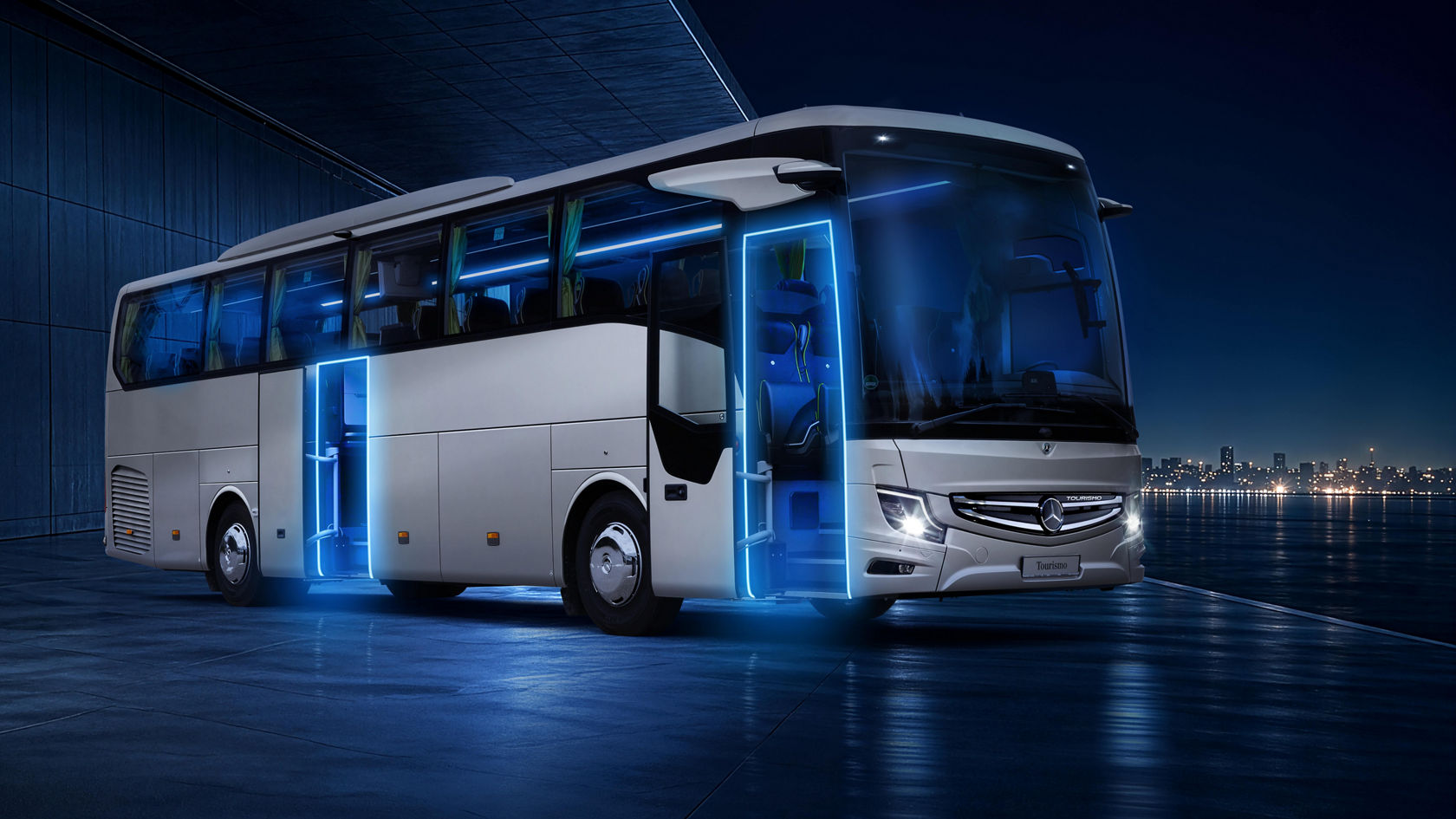 Mercedes-Benz Tourismo touring coach at night, with blue illuminated entrances and open doors, in the distance light silhouette of a city