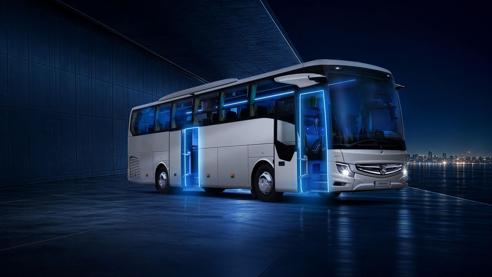 Mercedes-Benz Tourismo touring coach at night, with blue illuminated entrances and open doors, in the distance light silhouette of a city