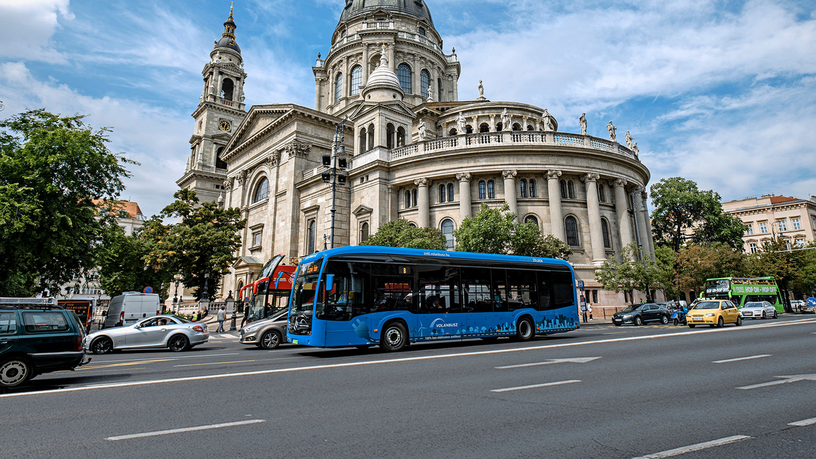 Modri mestni avtobus Mercedes-Benz eCitaro vozi v mestnem prometu po večpasovni cesti pred zgodovinsko kupolo 