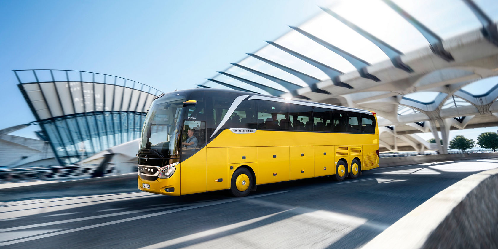 L'autobus da turismo Setra giallo viaggia davanti a un'architettura moderna alla luce del giorno